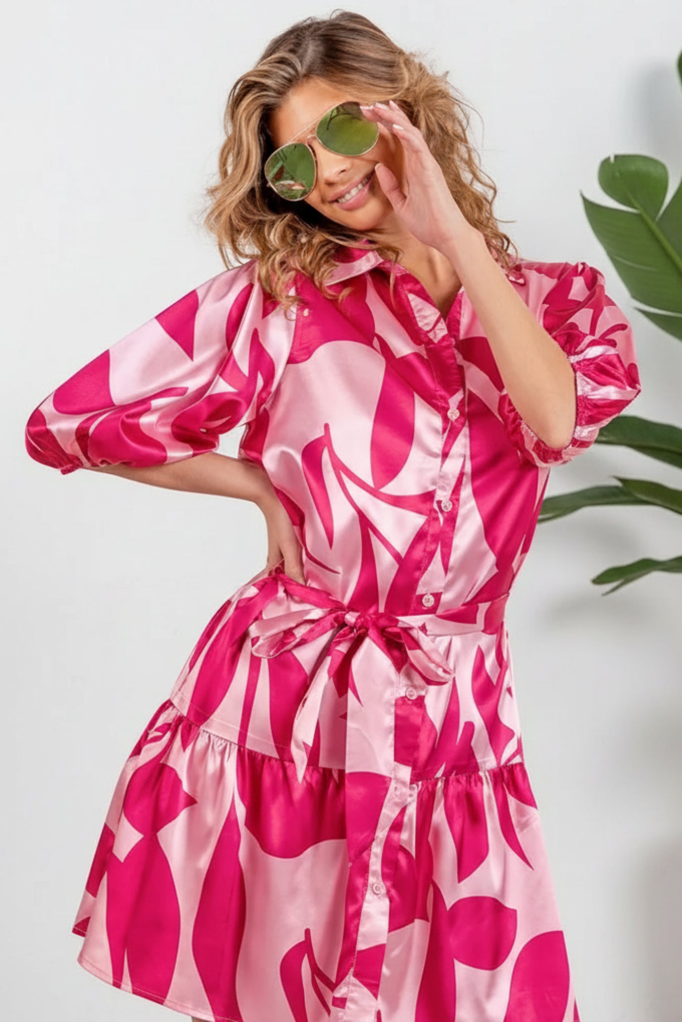 Woman wearing a pink and white patterned dress with sunglasses on a white background