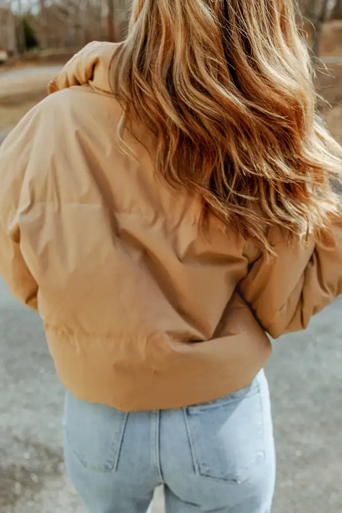 Person wearing a beige puffer jacket and light blue jeans outdoors