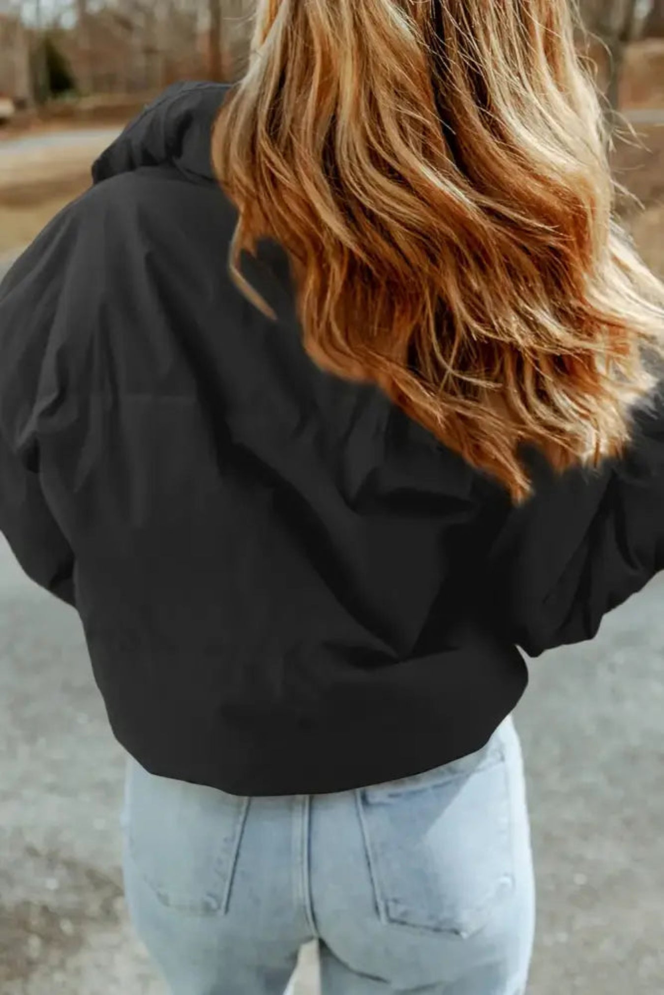Person wearing a black puffer jacket and light blue jeans outdoors