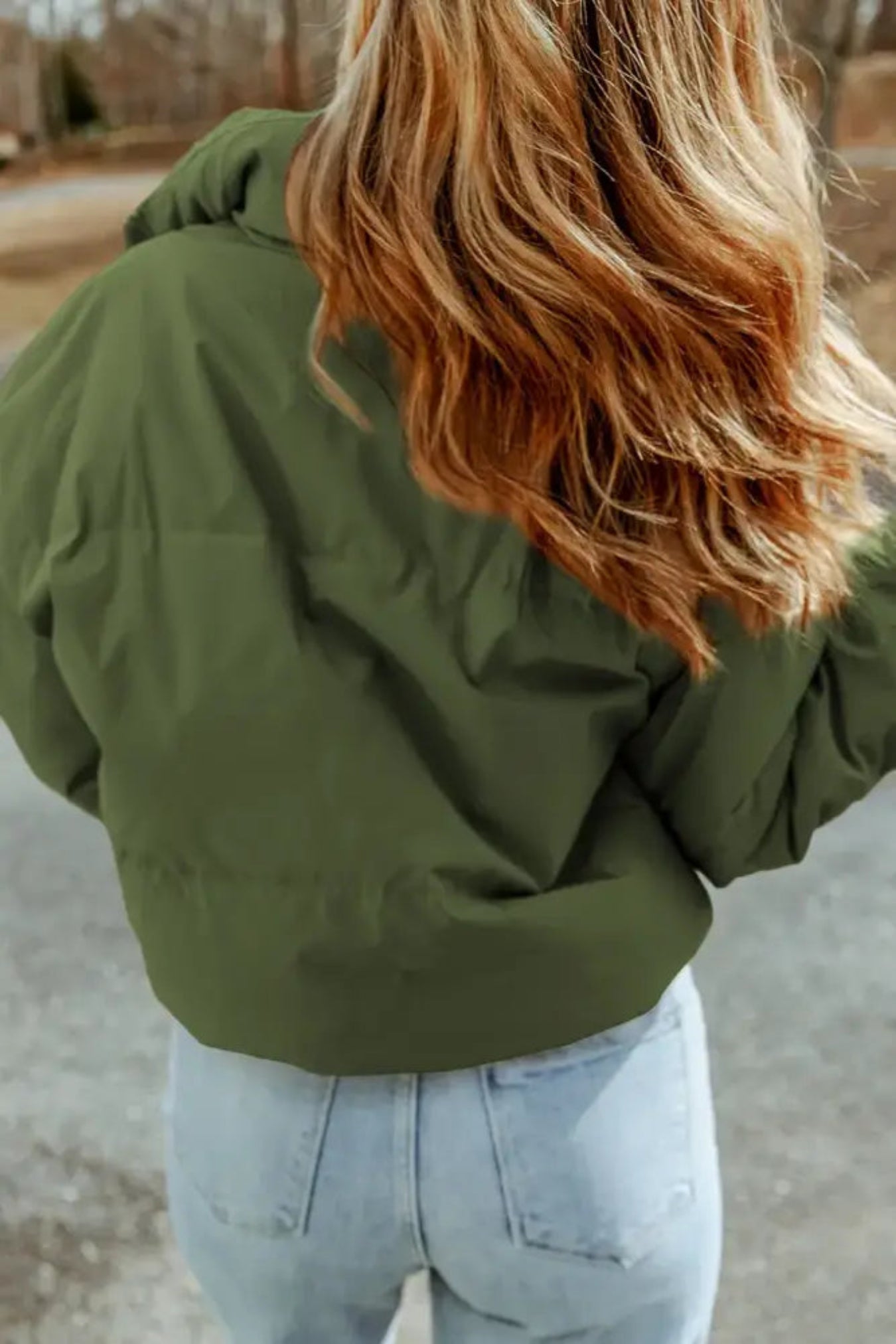 Person wearing a green puffer jacket and light blue jeans outdoors