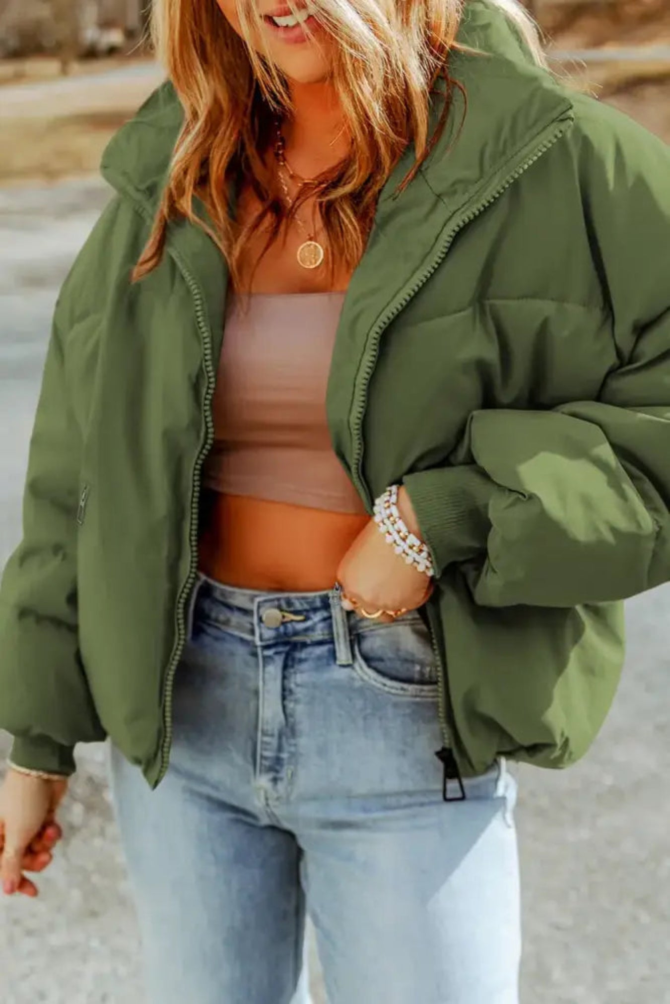 Person wearing a green puffer jacket and light blue jeans outdoors