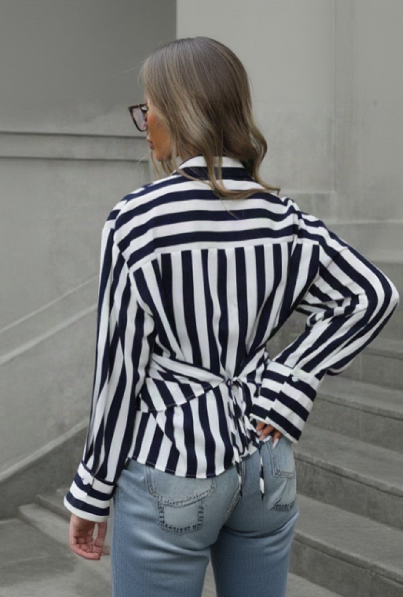 Person wearing a navy and white striped shirt with a tie waist, standing against a gray wall.