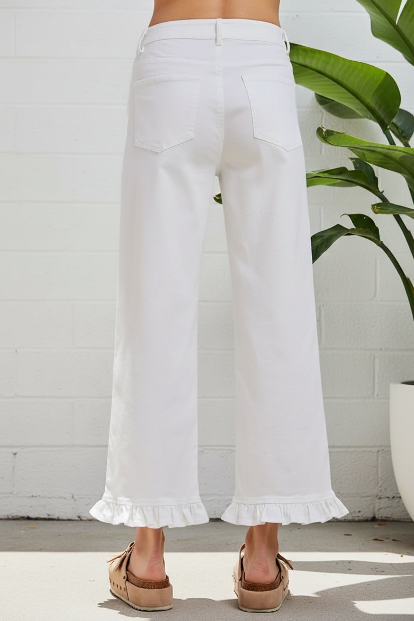 White cropped wide-leg jeans with a ruffled hem, shown from the back on a model wearing brown espadrille sandals against a white background.