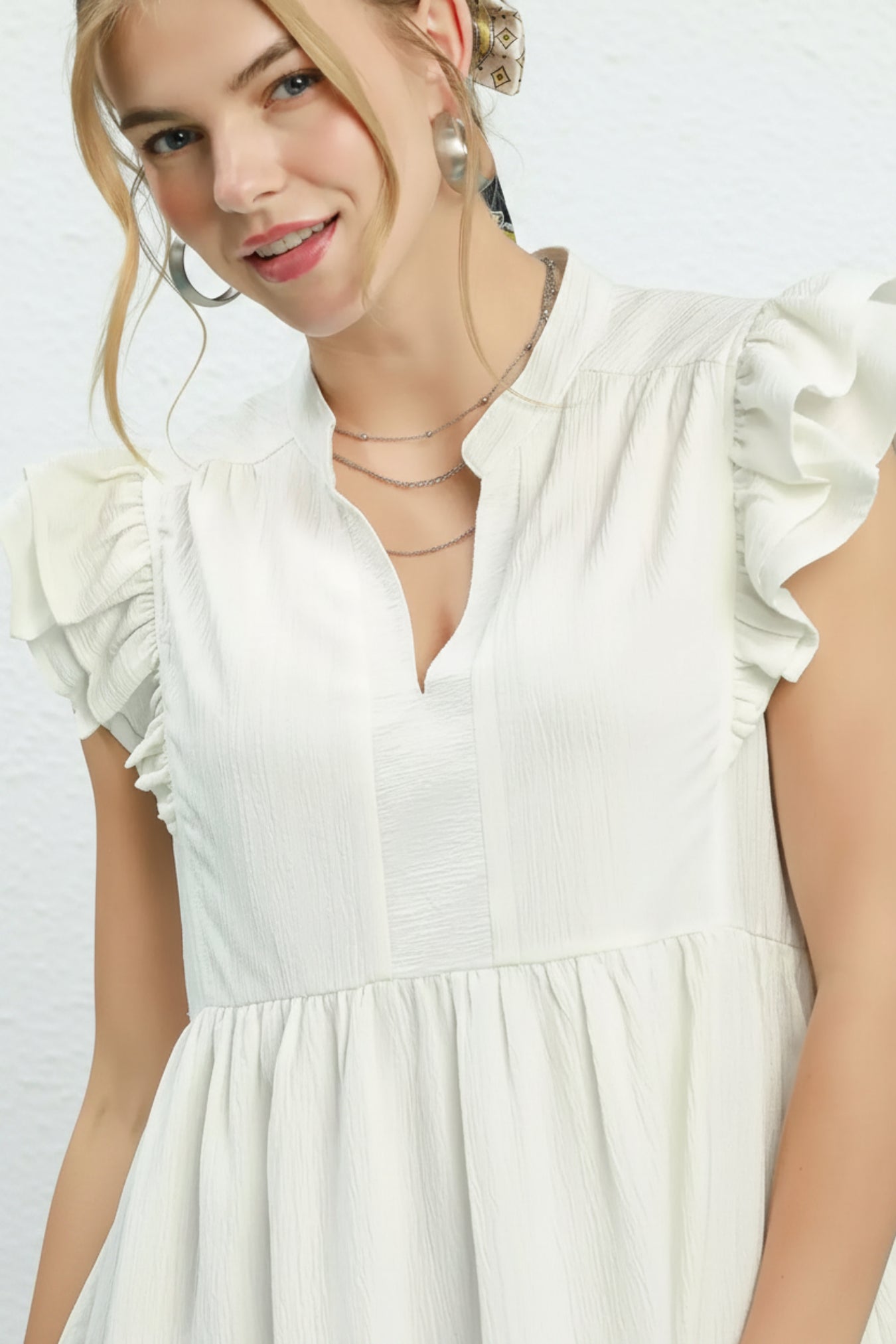 Woman wearing a white dress with ruffled sleeves against a white background
