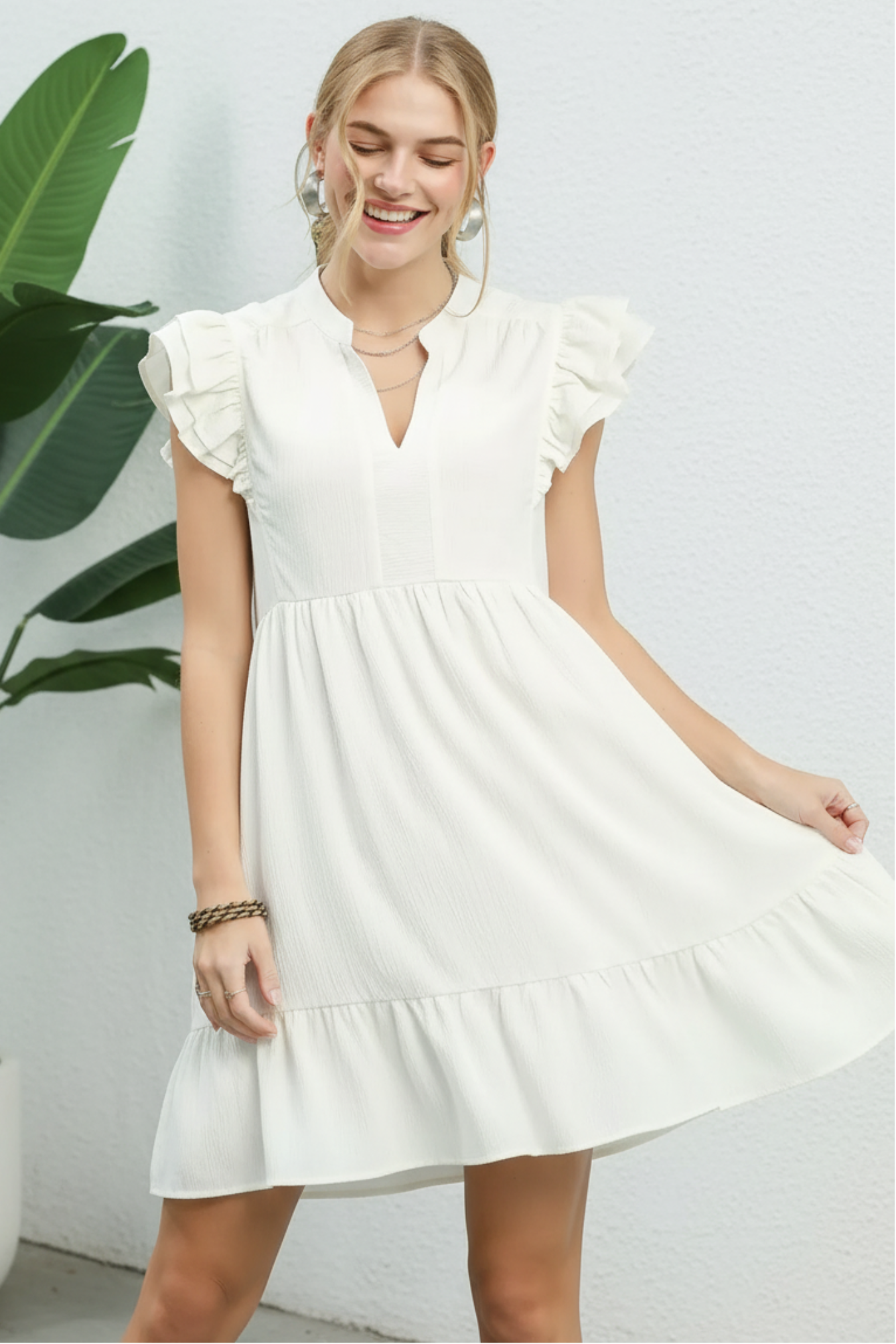 Woman wearing a white dress with ruffled sleeves against a white background