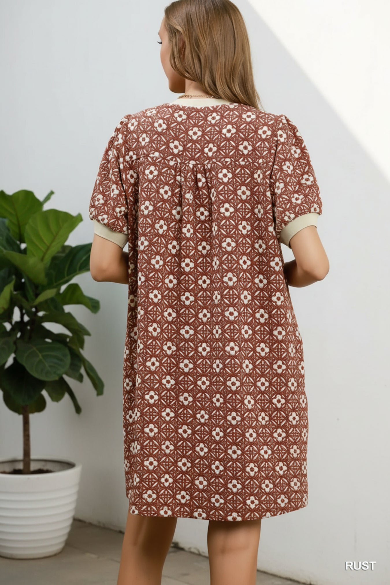 Woman wearing a rust-colored dress with floral pattern against a white background