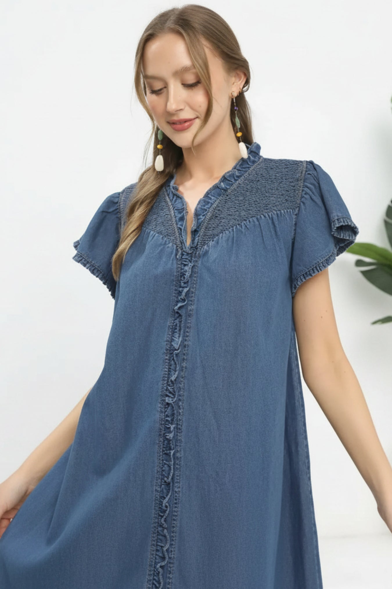 Woman wearing a blue denim dress with ruffled sleeves on a white background