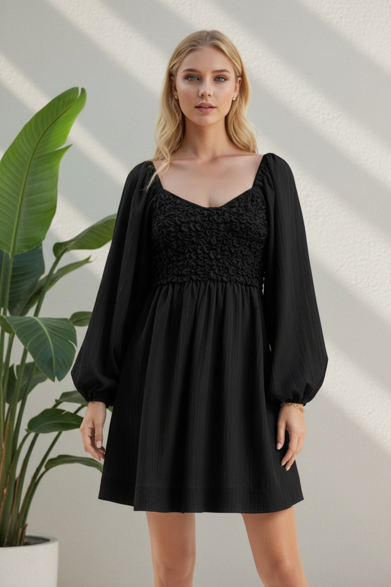A woman modeling a black mini dress with a smocked bodice, square neckline, and voluminous long balloon sleeves against a neutral studio background.