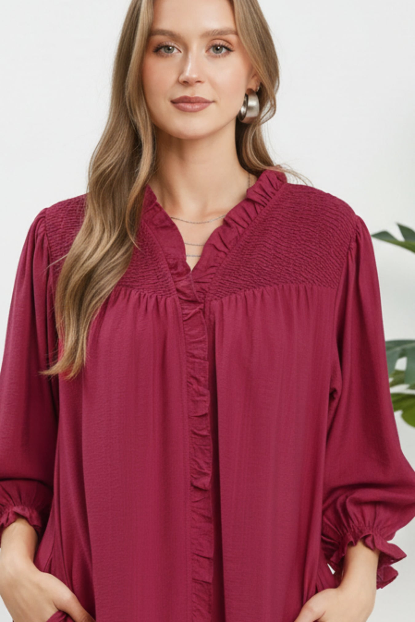 Woman wearing a maroon blouse with smocked details on a white background