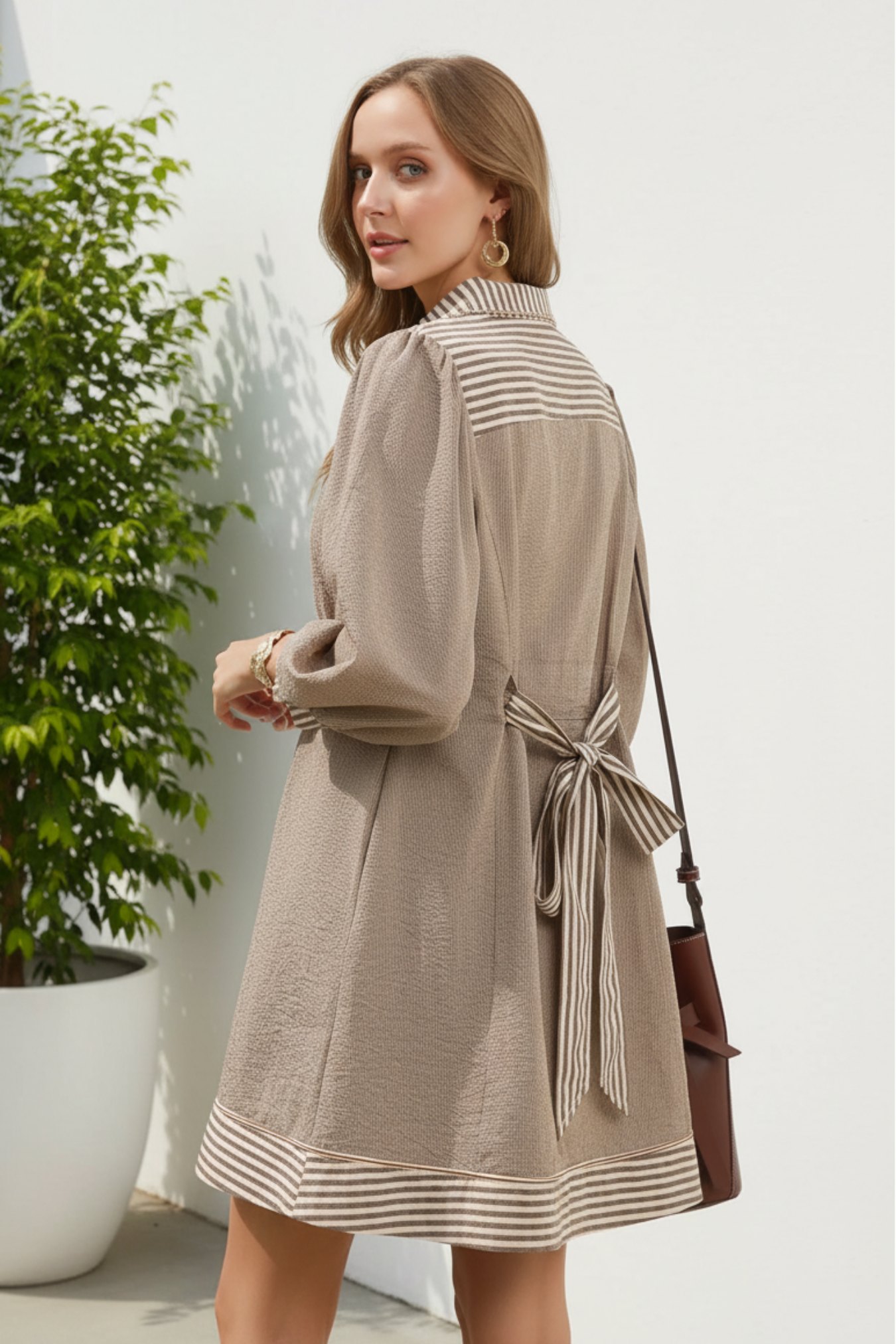 Woman wearing a brown dress with striped details against a white background