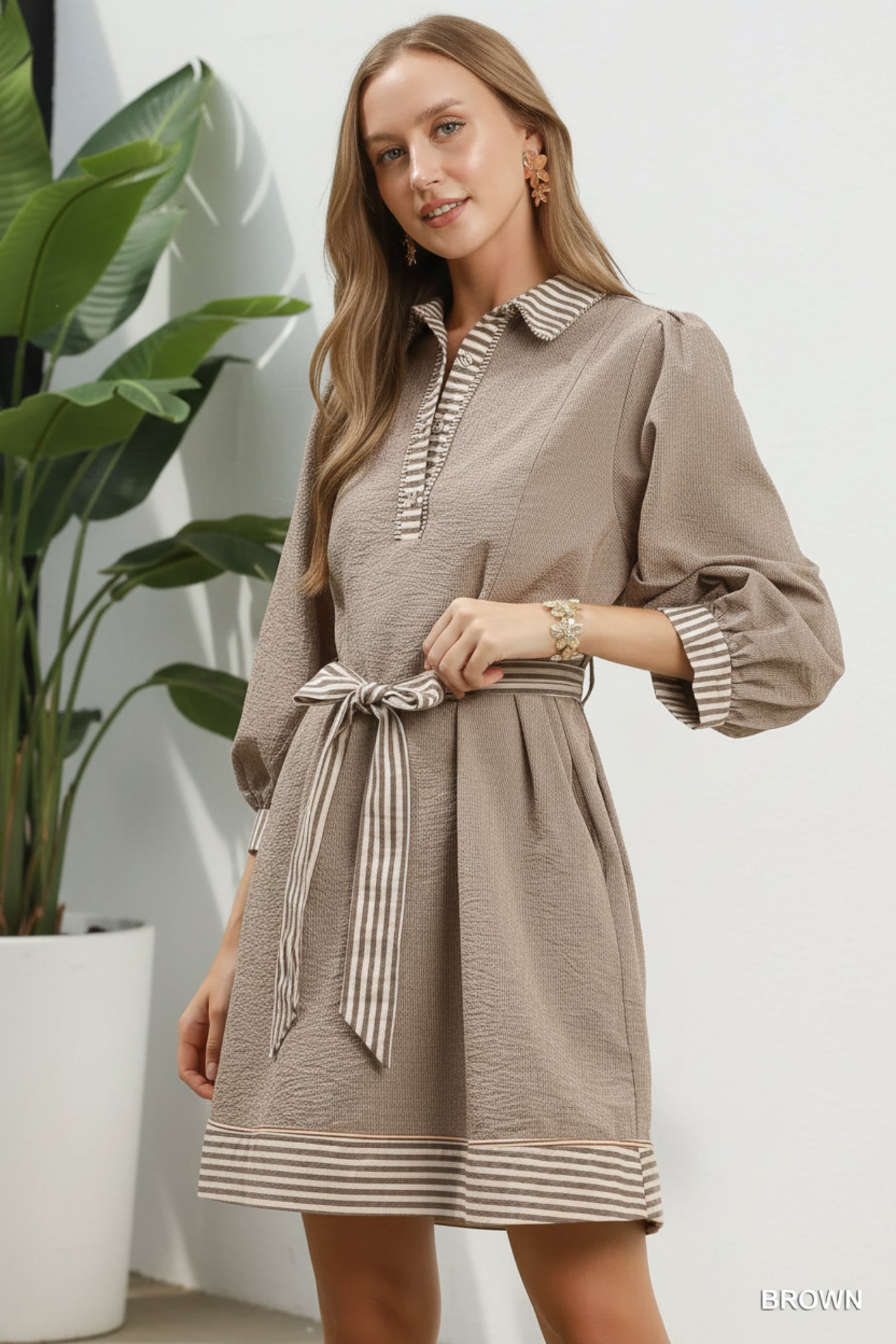 Woman wearing a brown dress with striped details against a white background