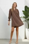 A woman modeling a brown short puff-sleeve dress against an olive green studio background. The dress has a gathered neckline and a loose, oversized silhouette.
