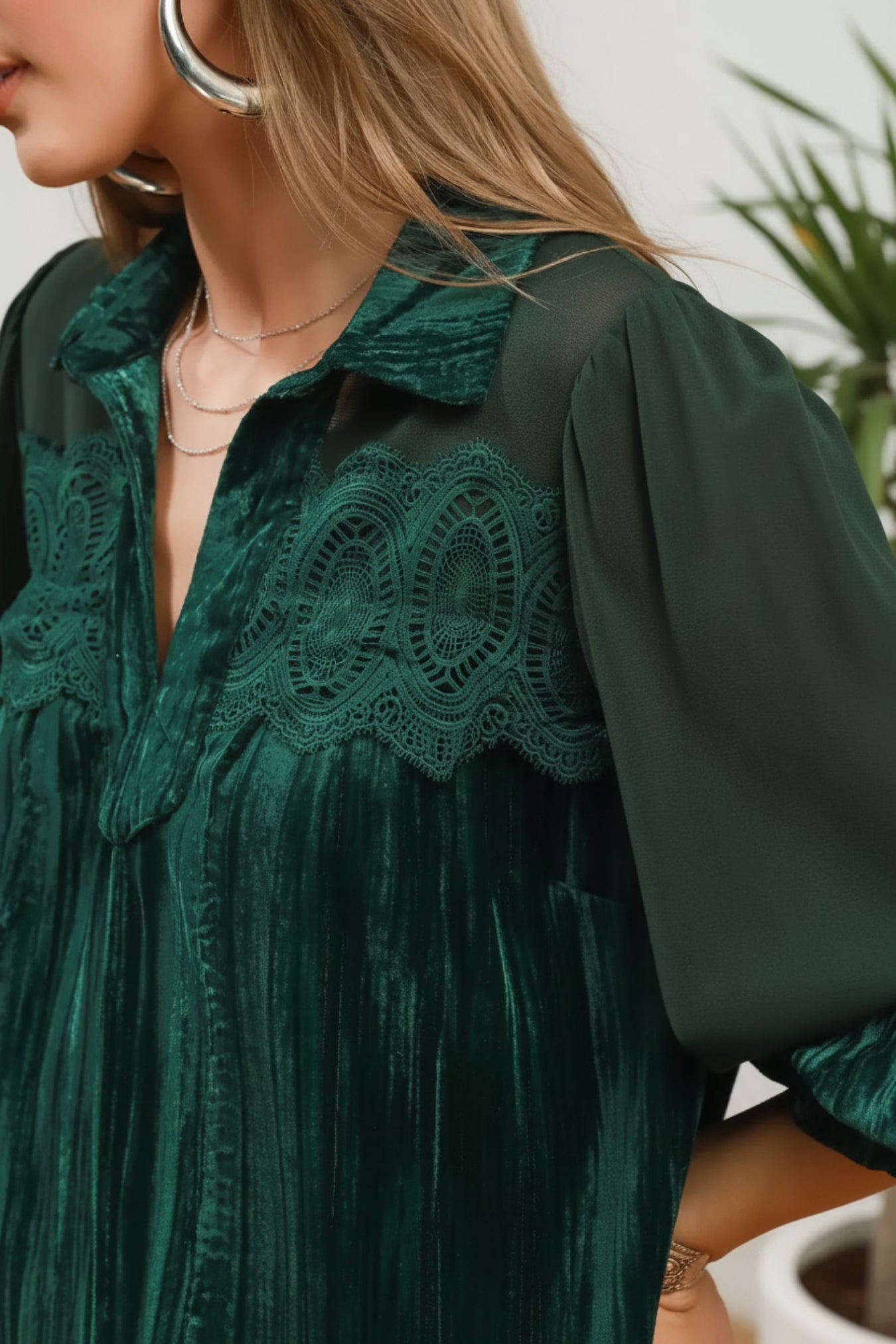 A close-up of a model wearing a dark emerald green velvet shirt dress with intricate lace embroidery across the chest and collar, set against a white background.