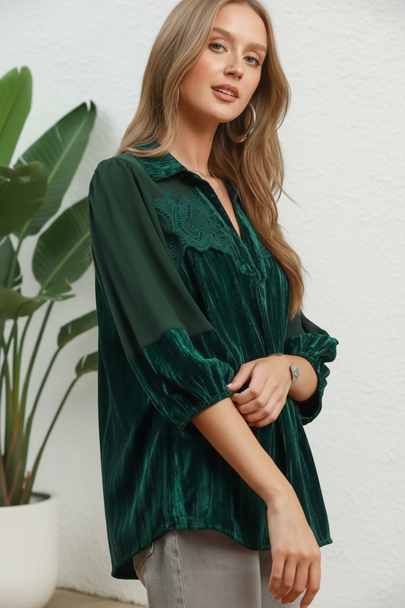 Woman wearing a hunter green blouse with lace details on a white background
