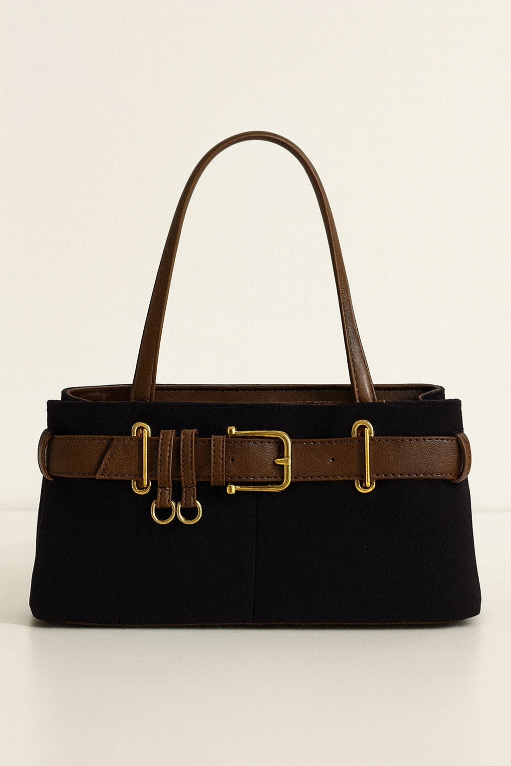Black handbag with brown leather strap and gold buckles on a beige background