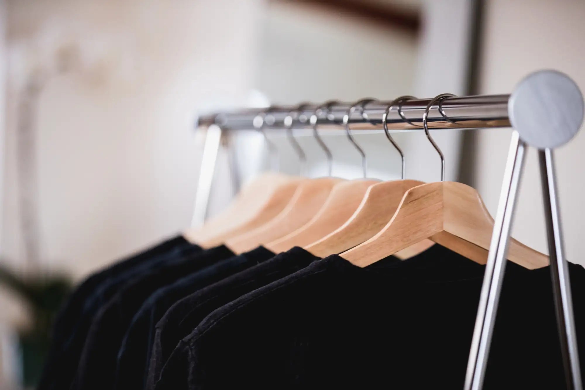 Chrome clothing rack with wooden hangers and black shirts.